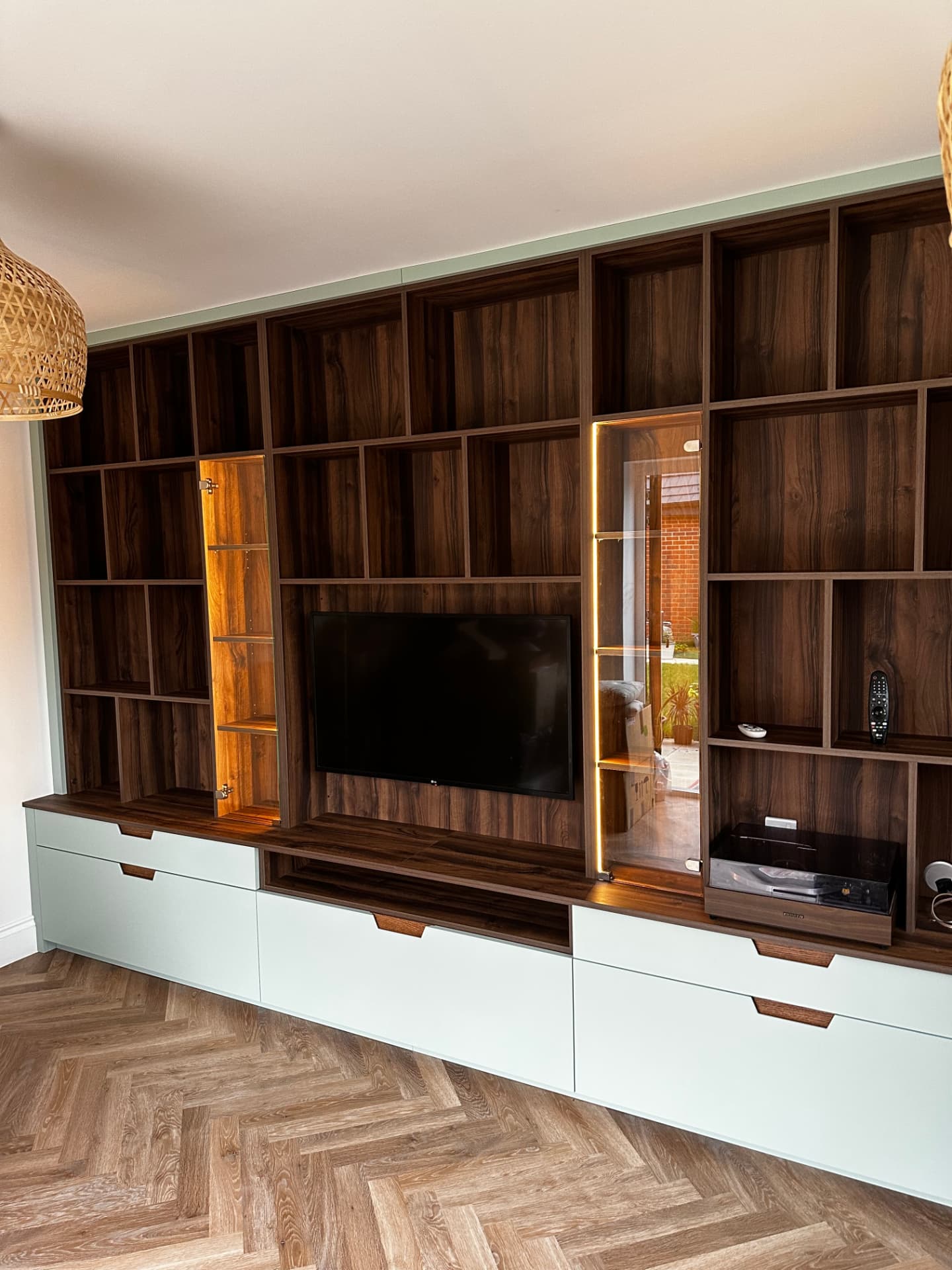 Bespoke dark wood media wall unit with mint green drawer fronts, integrated TV and lit display cabinets