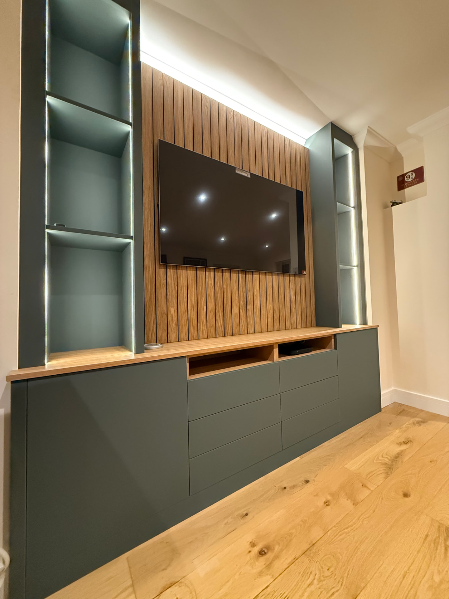 Dark green media wall with oak slatted panelling and concealed lighting